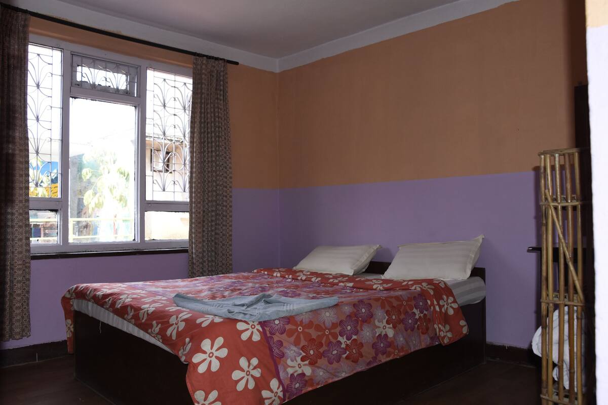 A bedroom with a bed, purple walls, and a window with curtains.
