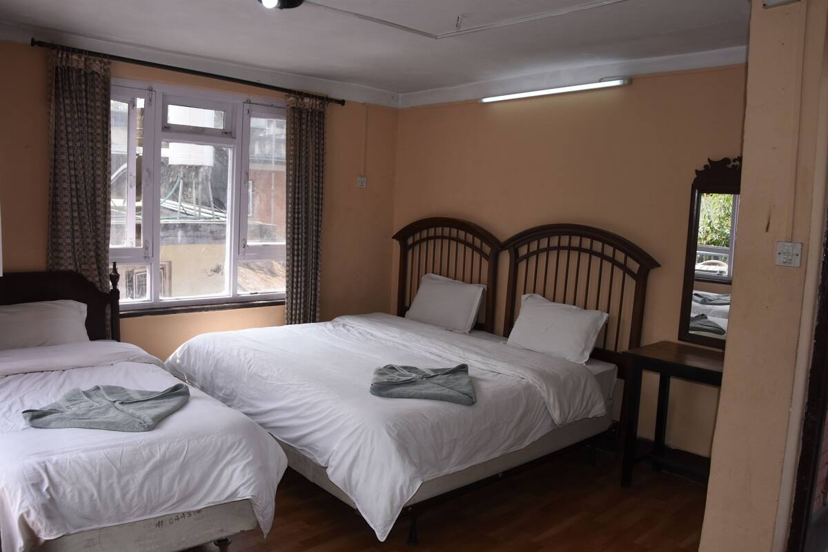 A bedroom with two single beds, a wooden headboard, a small table, and a window with curtains.