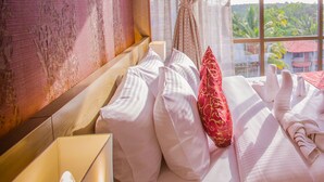 Une chambre d’hôtel avec un grand lit, une tête de lit en bois, une fenêtre donnant sur un paysage verdoyant et un rideau.