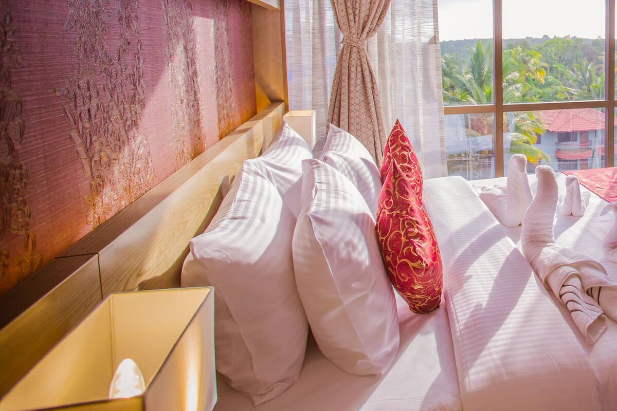 Ein Hotelzimmer mit einem großen Bett, einem Holzkopfende, einem Fenster mit Blick ins Grüne und einem Vorhang.