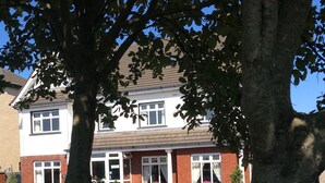 A two-story house with a brick facade, white windows, and a front garden with pink flowers. - Westwinds (Galway)