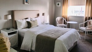 A hotel room with a large bed, two bedside tables with lamps, a small round table, two chairs, and a window with curtains. - Westwinds (Galway)
