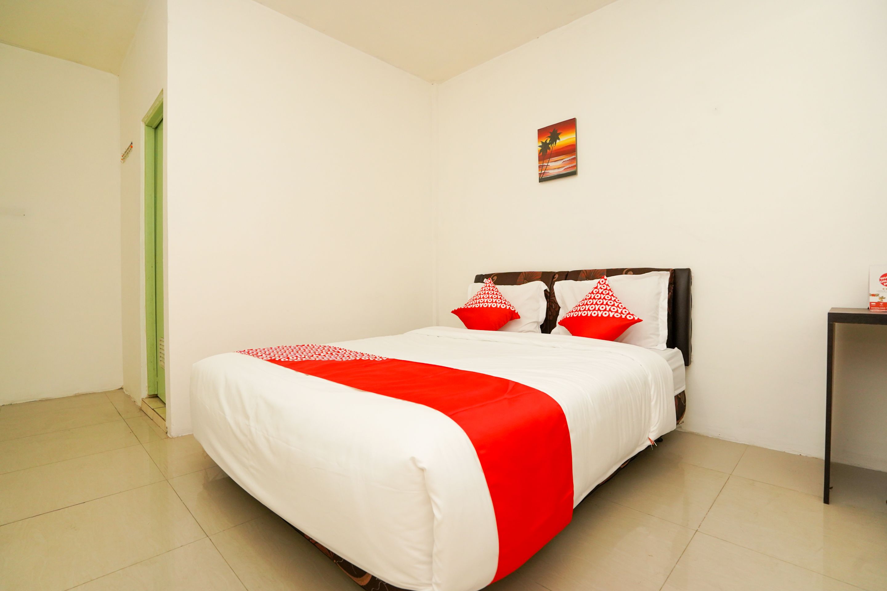 Una cama bien hecha con una colcha blanca y roja, un cabecero de madera y dos almohadas rojas con letras blancas.