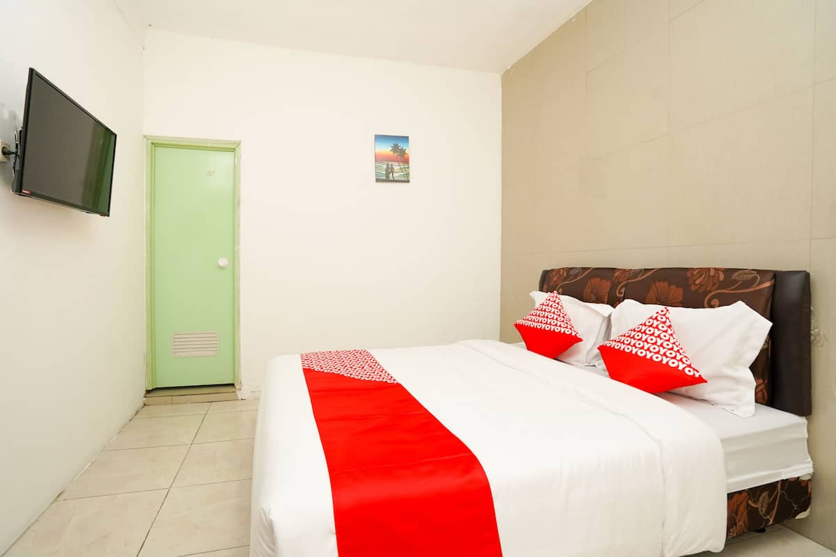 Una habitación de hotel con una cama, una puerta verde, un televisor de pantalla plana y un cuadro pequeño en la pared.