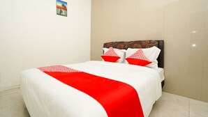Un lit bien fait, recouvert d’une couverture rouge et blanche, avec deux oreillers à motifs rouges et blancs, et un petit tableau encadré accroché au mur.