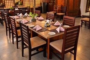 Un comedor con mesas y sillas de madera, dispuesto ordenadamente con platos, cubiertos y servilletas.