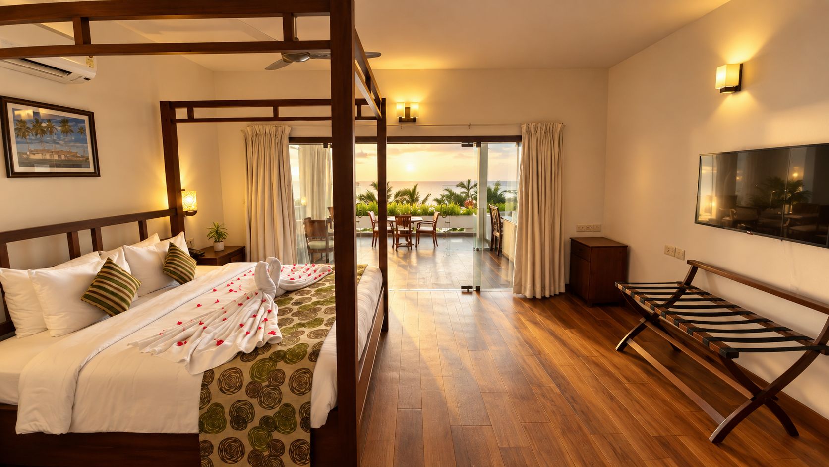 A hotel room with a four-poster bed, a flat-screen TV, a wooden bench, and a balcony with a view of the ocean.