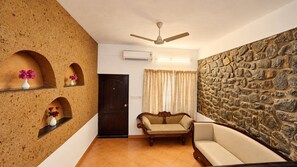 Una sala de estar con pared de piedra, puerta de madera, un sofá, un banco de madera y un ventilador de techo.