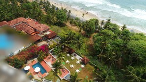 Vista aérea de un complejo turístico con zona de piscina, mobiliario exterior y playa.