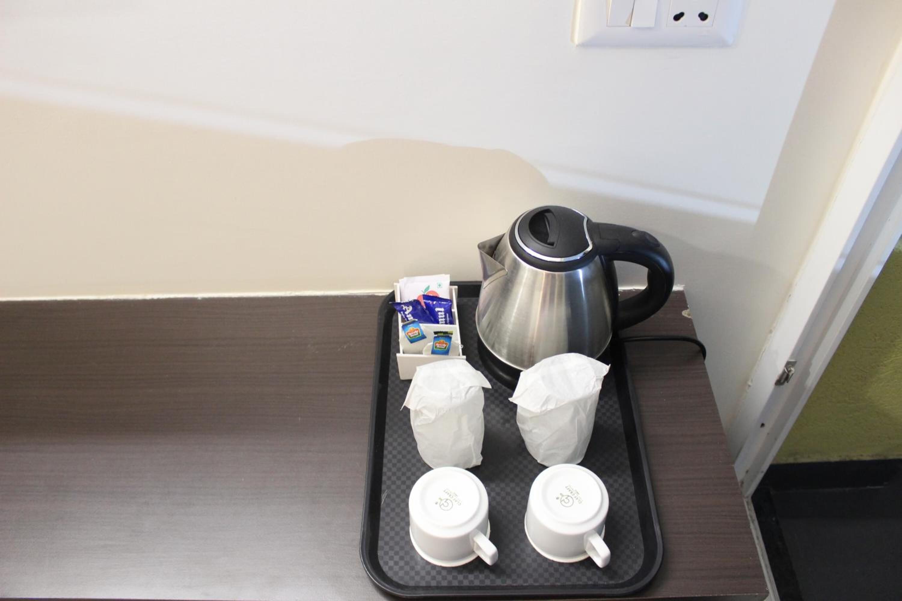 A tray with a coffee pot, two cups, and a box of tissues on a dark countertop.