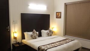 A neatly made bed with a headboard, two bedside lamps, and a bedside table with a phone. - Hotel Sai (Bawal)