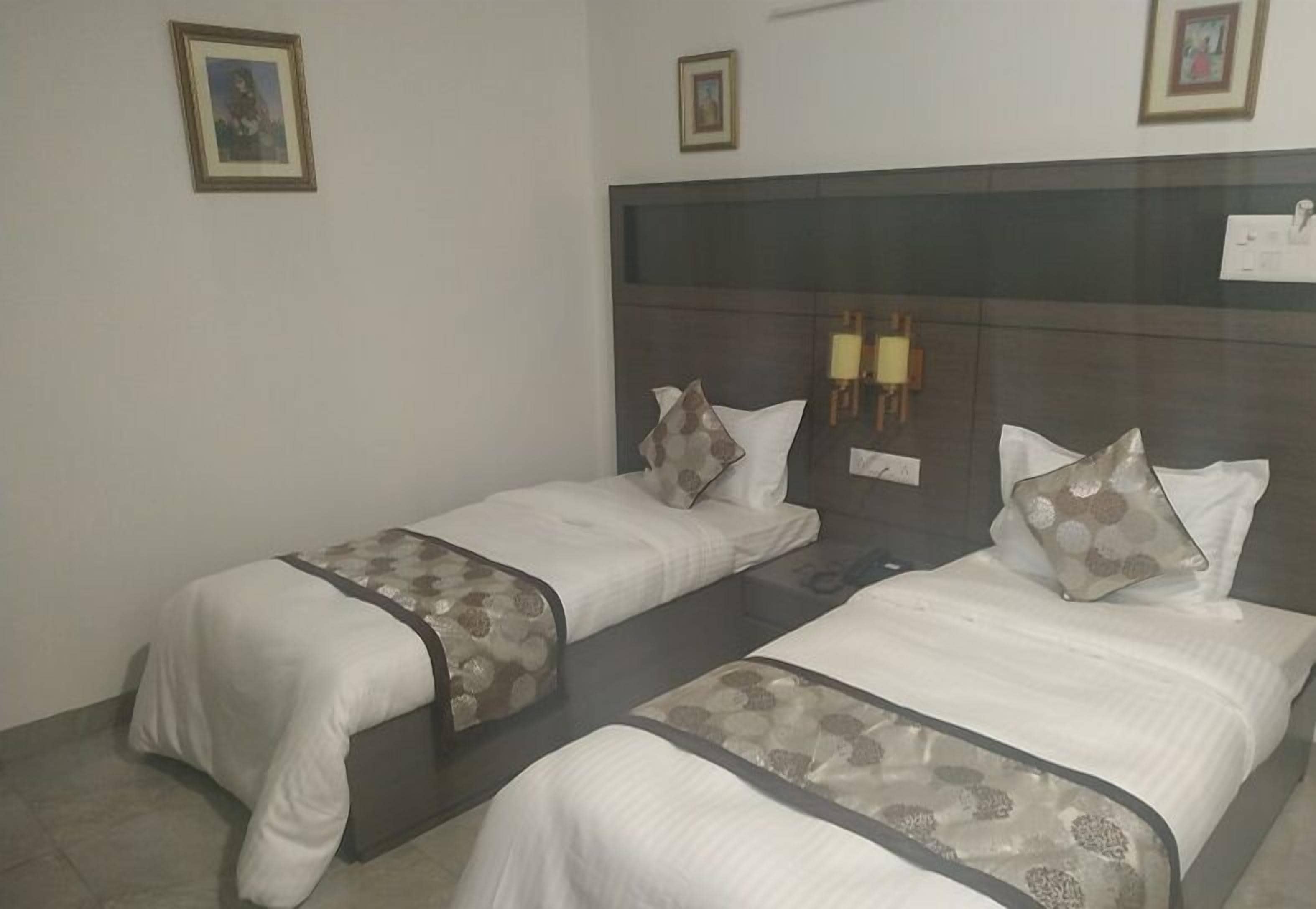 A hotel room with two single beds, each with a patterned bedspread and pillows, a dark headboard, and framed pictures on the walls.