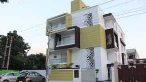 A modern multi-story residential building with a gated entrance, a balcony, and a parking area with two cars. - Hotel Sai (Bawal)