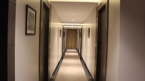 A modern hotel hallway with a carpeted floor, framed artwork on the walls, and doors leading to rooms. - Hotel Sai (Bawal)