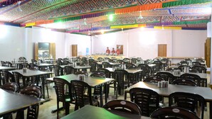 Une grande salle à manger avec de nombreuses tables et chaises, un plafond décoré et une scène où se trouvent des personnes.
