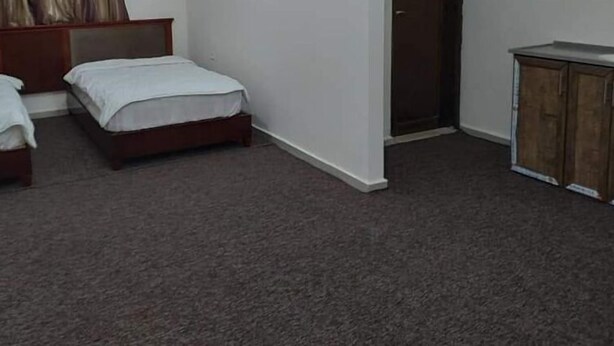 A room with two single beds, a wooden wardrobe, and a carpeted floor. - Alwalajy towers (Jericho)