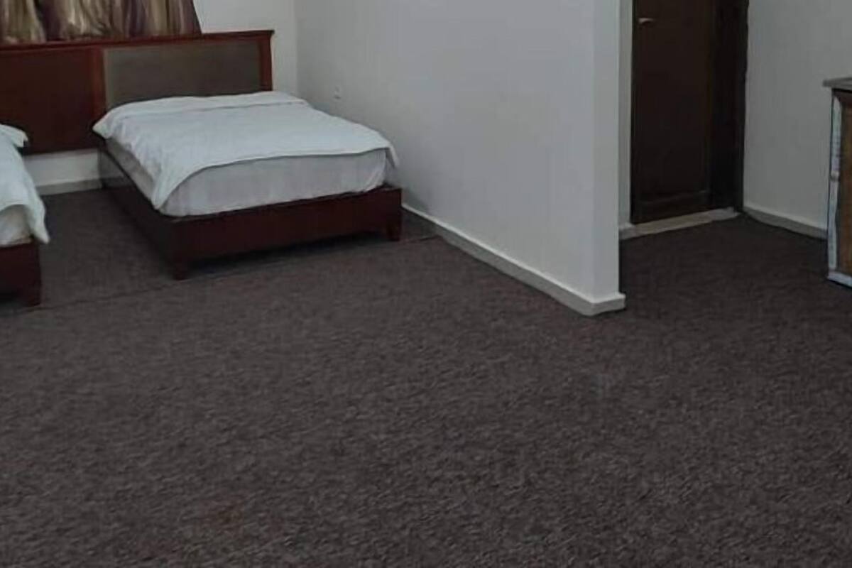 Una habitación con dos camas individuales, un armario de madera y suelo alfombrado.