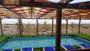 A pool area with blue lounge chairs, a wooden pergola, and a view of the cityscape. - Alwalajy towers (Jericho)