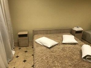 A hotel room with a bed, two pillows, a nightstand, a wooden headboard, and a patterned floor. - Arcobaleno Home - Hostel (Kyiv)
