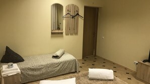 Une petite chambre à coucher accueillante, avec un lit simple, un tapis moelleux, une table de chevet avec une lampe et un miroir au-dessus du lit.