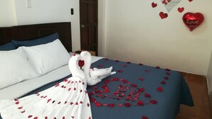 A bed with a blue bedspread, white pillows, and a white towel arranged in a swan shape with rose petals. - Kasas del Inka Machupicchu (Machu Picchu)