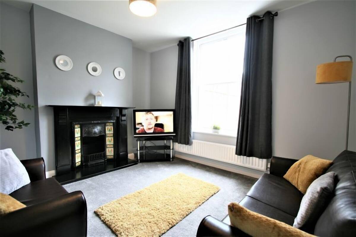 A living room with a fireplace, a television, and a large window with curtains.