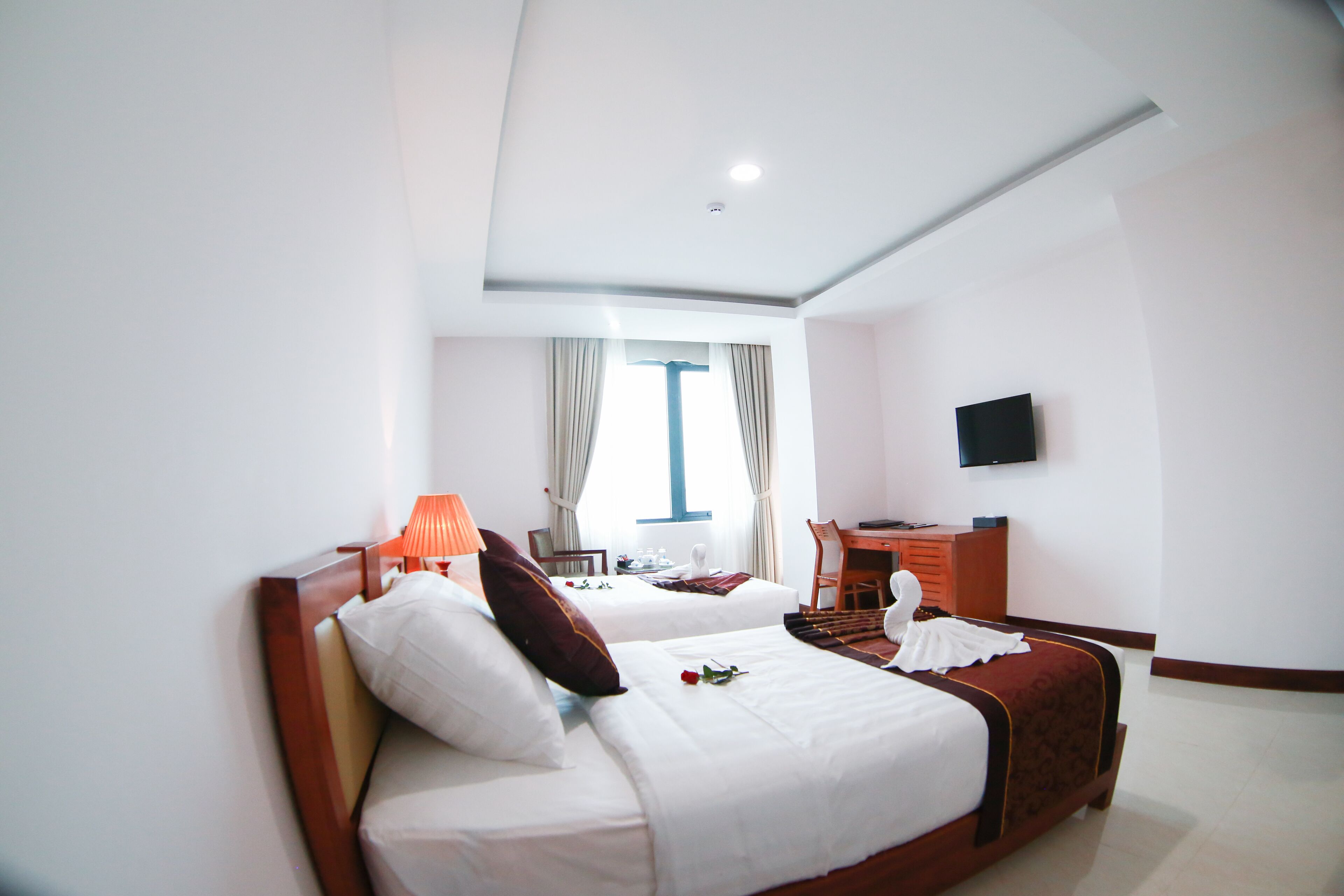 A hotel room with two beds, a desk, a chair, a television, and a window with curtains.