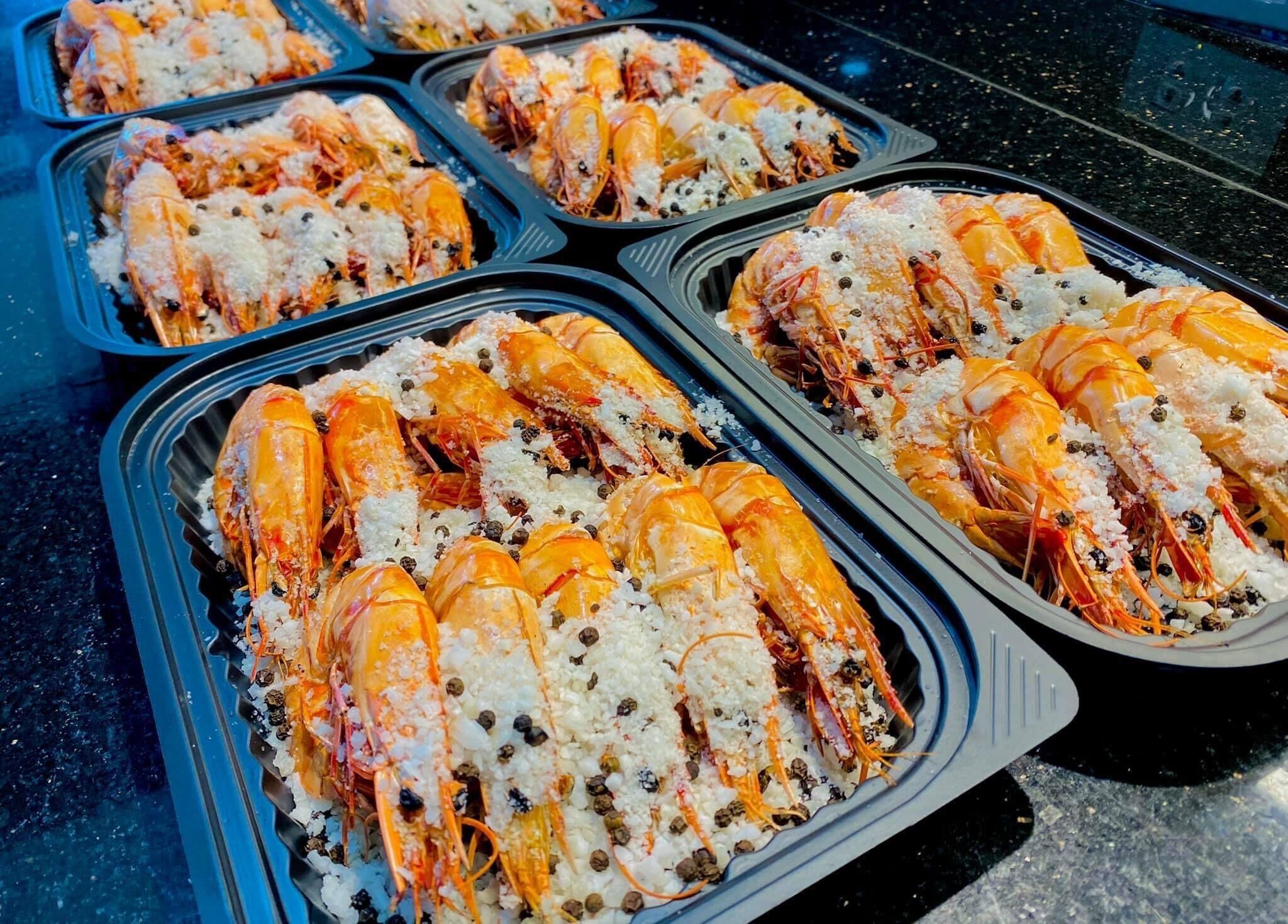 Trays of cooked shrimp garnished with herbs and spices.
