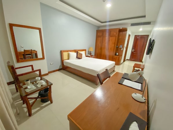 Habitación de hotel con cama, escritorio, silla, armario y espejo.