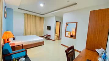 A hotel room with a bed, a desk, a chair, a table with cups, a lamp, and a mirror.