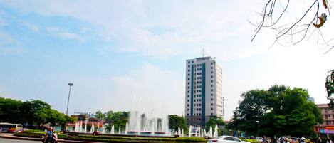 A busy urban intersection with a fountain, a tall building, and various vehicles.