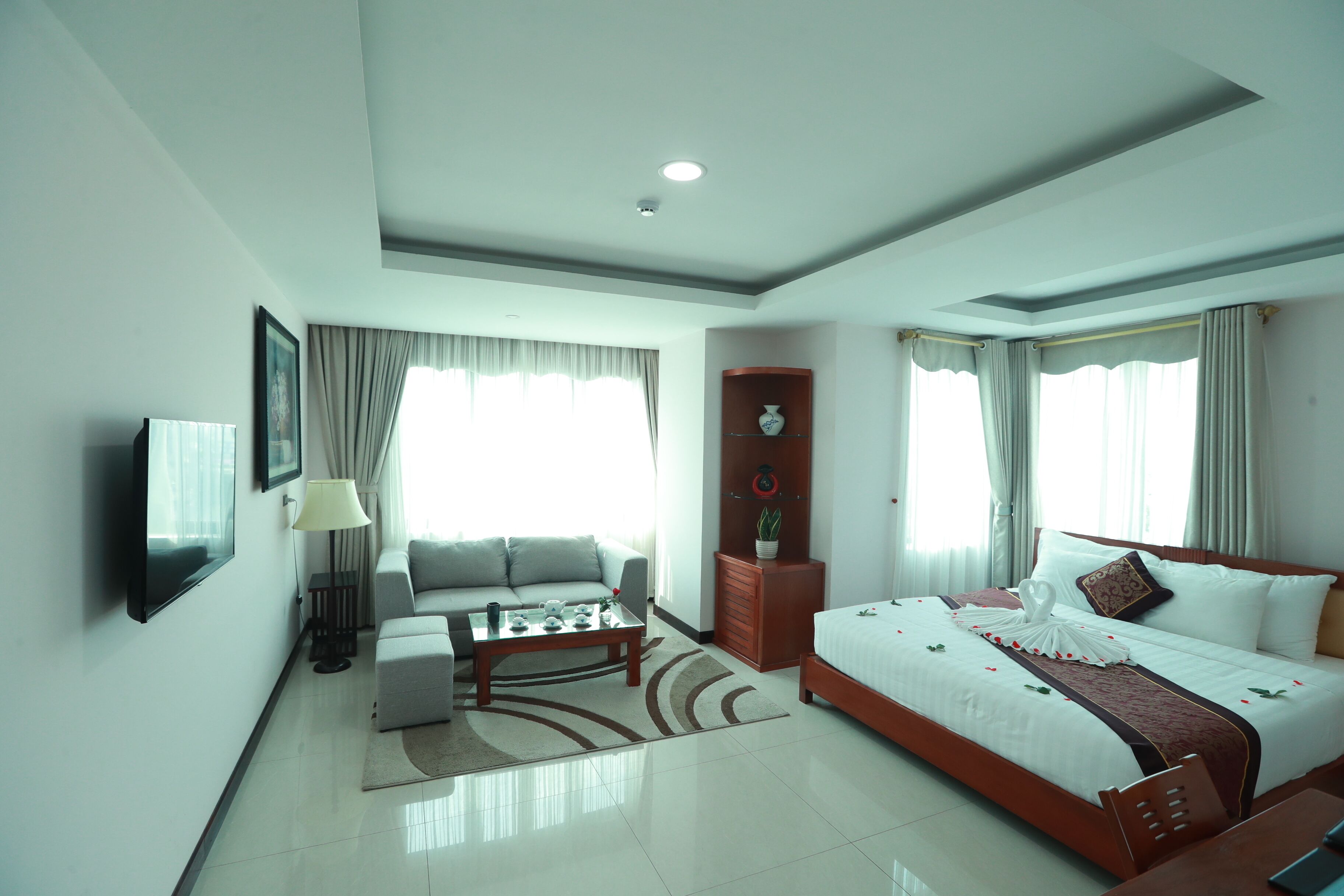 Una habitación de hotel moderna con una cama, sofá, mesa de centro y una televisión montada en la pared.
