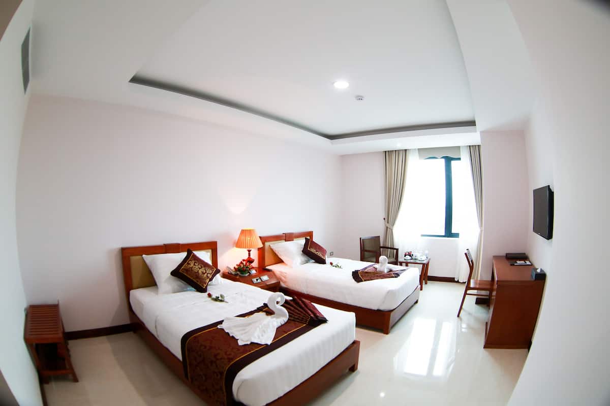 Habitación de hotel con dos camas, un escritorio, una silla, un televisor y una ventana con cortinas.