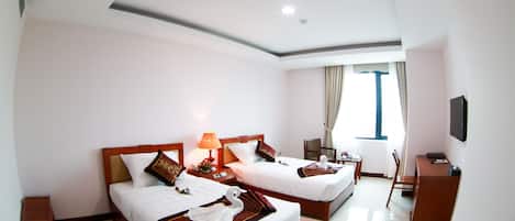 A hotel room with two beds, a desk, a chair, a TV, and a window with curtains.