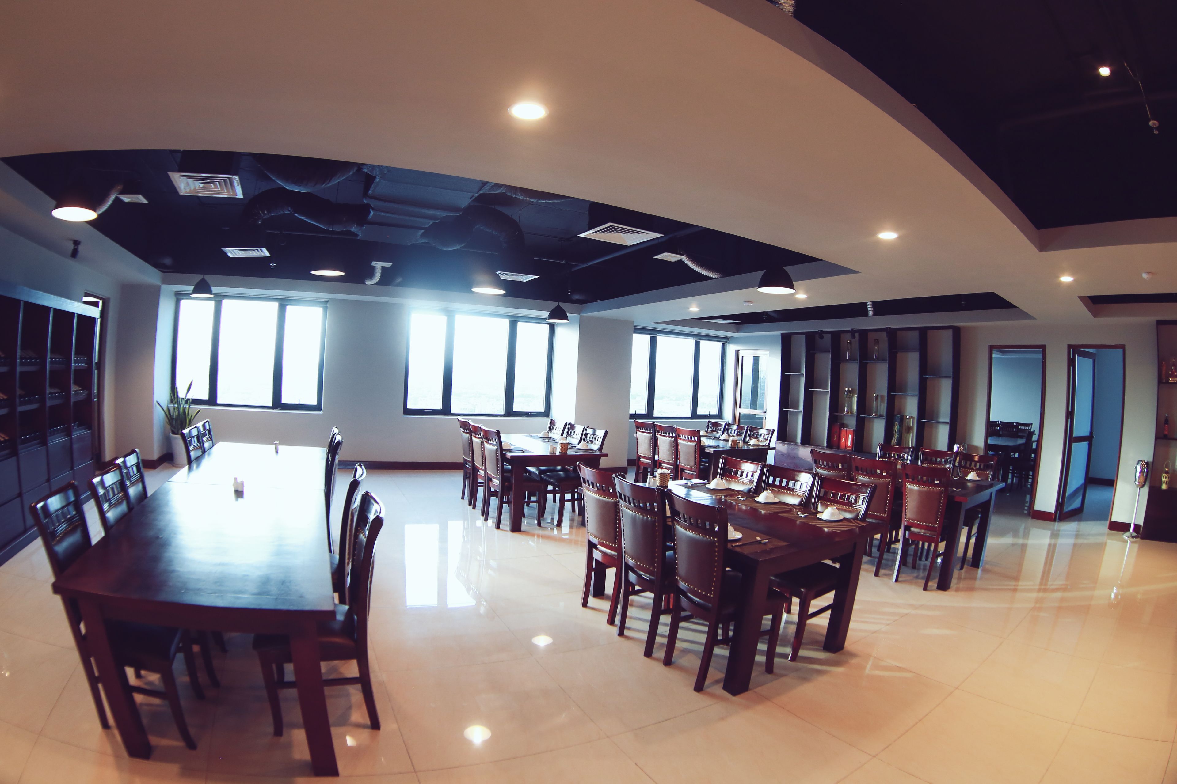 A spacious conference room with multiple tables and chairs, large windows, and a high ceiling with exposed ductwork.