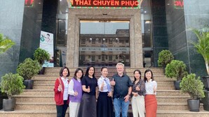Un groupe de personnes posant devant un bâtiment sur lequel on peut lire l’inscription « THAI CHUYEN PHUONG ».