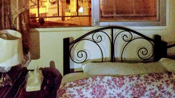 A room with a bed, a window with decorative ironwork, and a view of a brightly lit interior space. - Youth guest house (Wadi Musa)