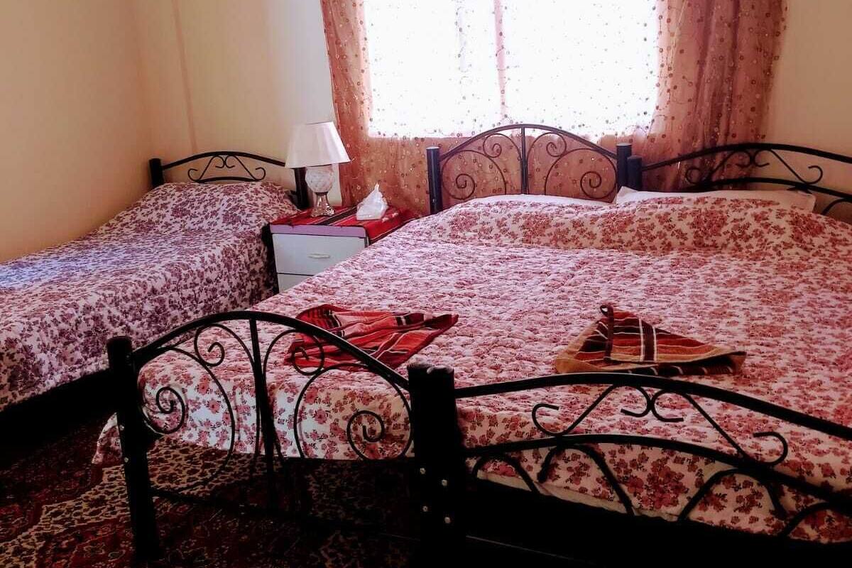 A bedroom with two beds, a nightstand, a lamp, and a window with curtains.