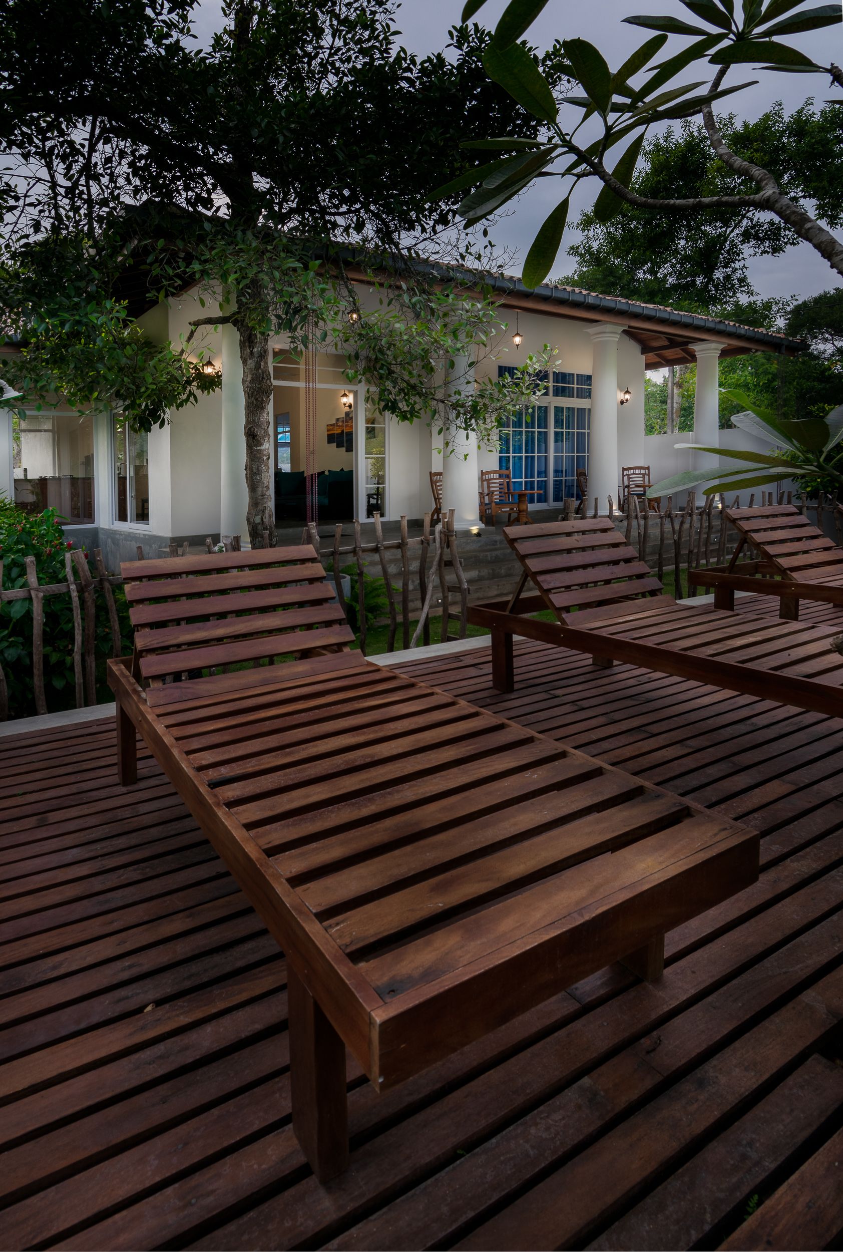 A wooden deck with lounge chairs, a building with large windows, and a tree in the background.