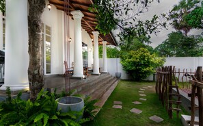 A covered outdoor area with a wooden ceiling, white columns, and a stone pathway leading to a seating area with chairs and tables. - Pearl Villa Welhengoda (Ahangama)