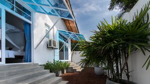 Una casa moderna con una escalera que conduce a un dormitorio, una planta grande en maceta y una pared exterior blanca.