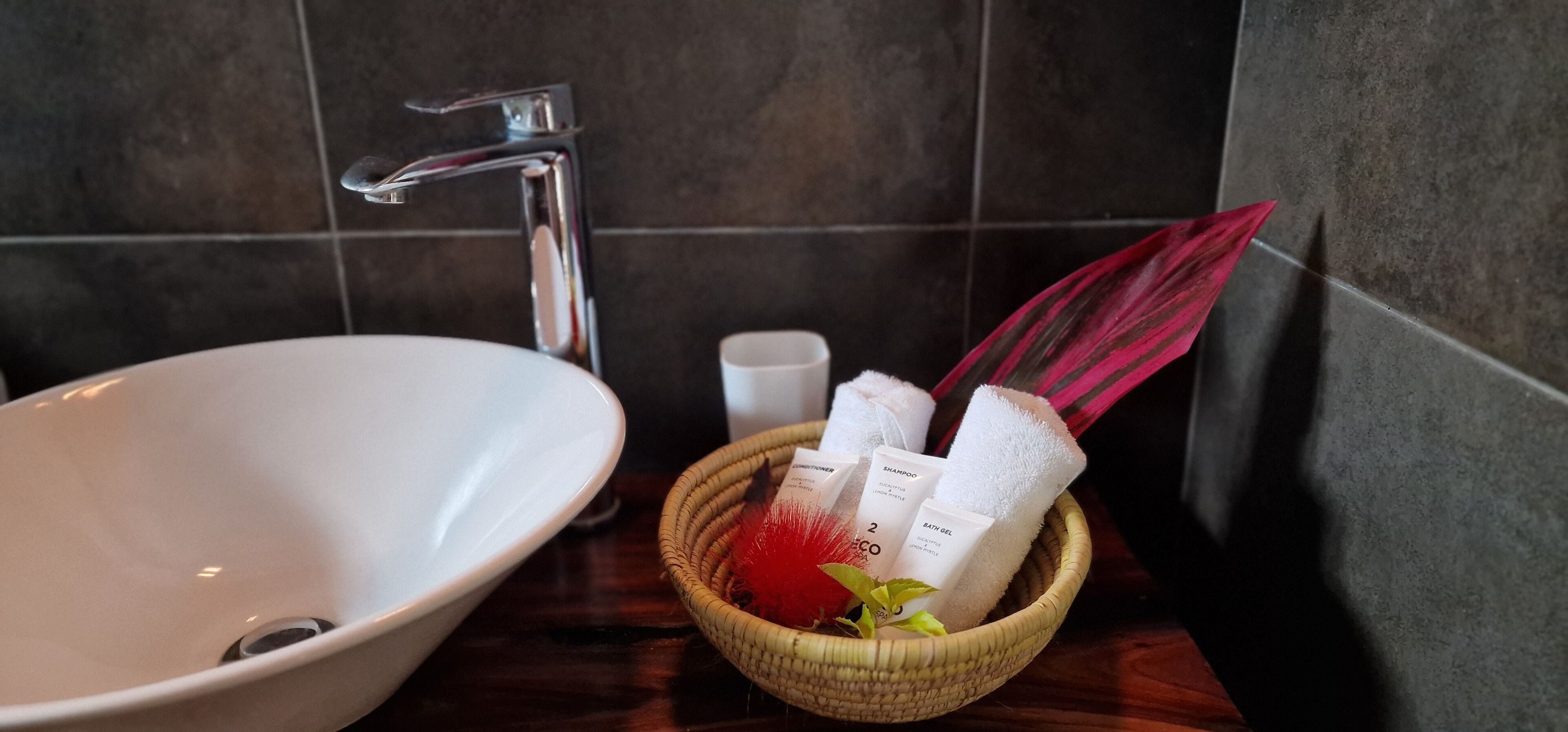 A bathroom sink with a chrome faucet, a small white cup, and a basket containing toiletries.