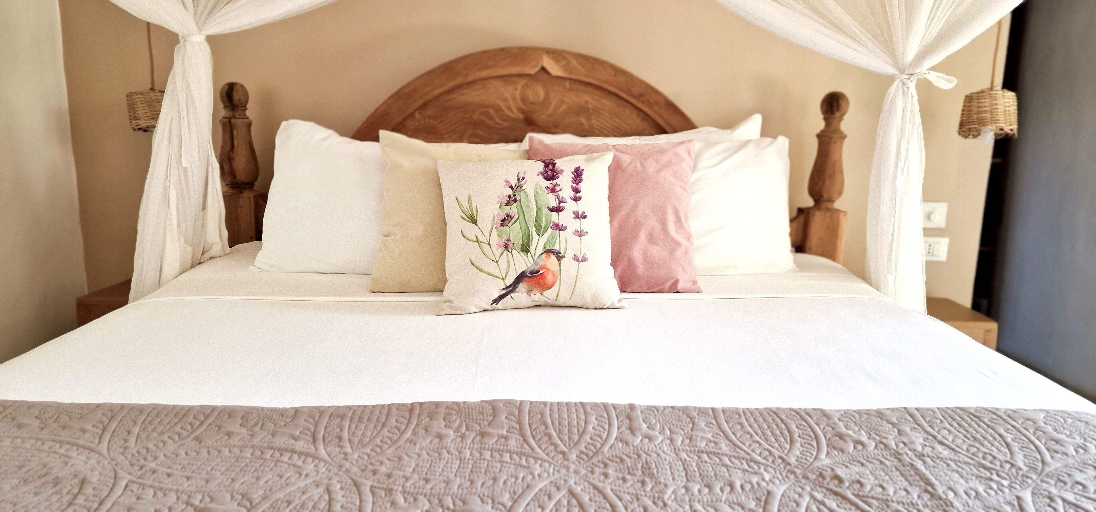 Ein Bett mit Holz-Kopfteil, weißer Bettwäsche und einem dekorativen Kissen mit floralem Muster.