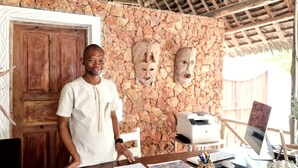 A reception desk with a stone wall background, wooden door, and a computer setup. - ARYA Boutique Resort (Kiwengwa)