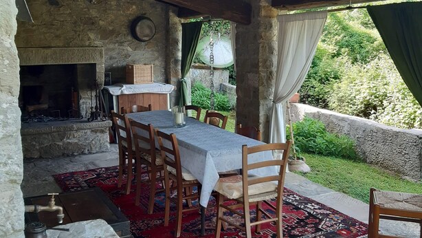 An outdoor dining area with a stone table and chairs, a rustic stone wall, and a view of greenery. - Country Residence Turicchi (Dicomano)