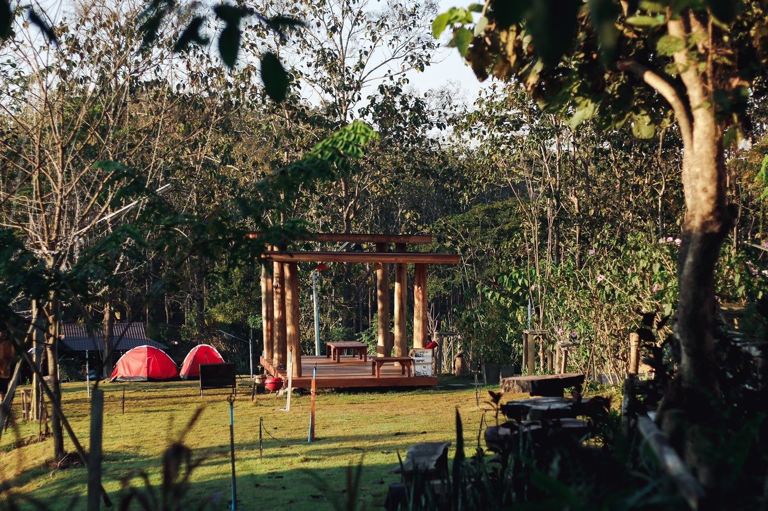 A gazebo in a wooded area with a picnic table and two red tents.