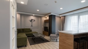 A modern living room with a green sofa, a glass coffee table, and a wooden dining area with bar stools. - On4 Rooms & Suites (Istanbul)