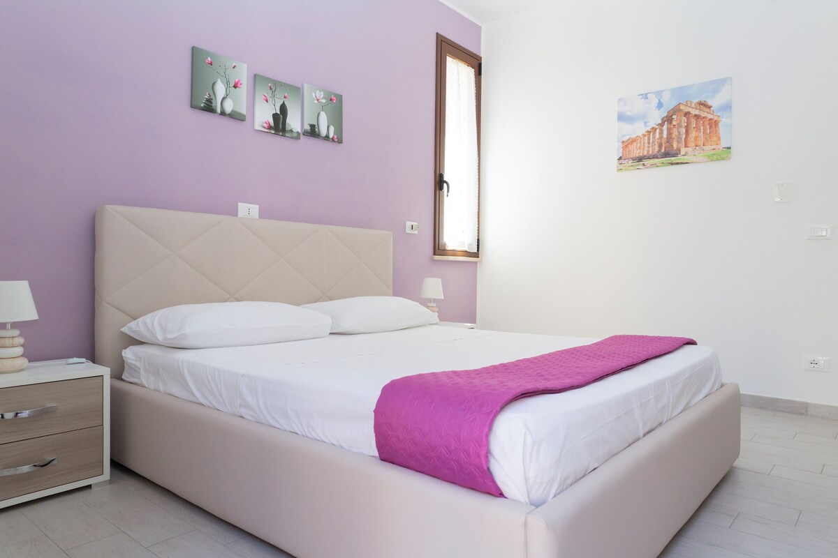 Une chambre à coucher avec un lit, une table de chevet, une fenêtre et des œuvres d’art murales.