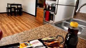 A compact kitchen with wooden cabinets, a stainless steel refrigerator, a microwave, and a sink. - Kingston East (Rexburg)