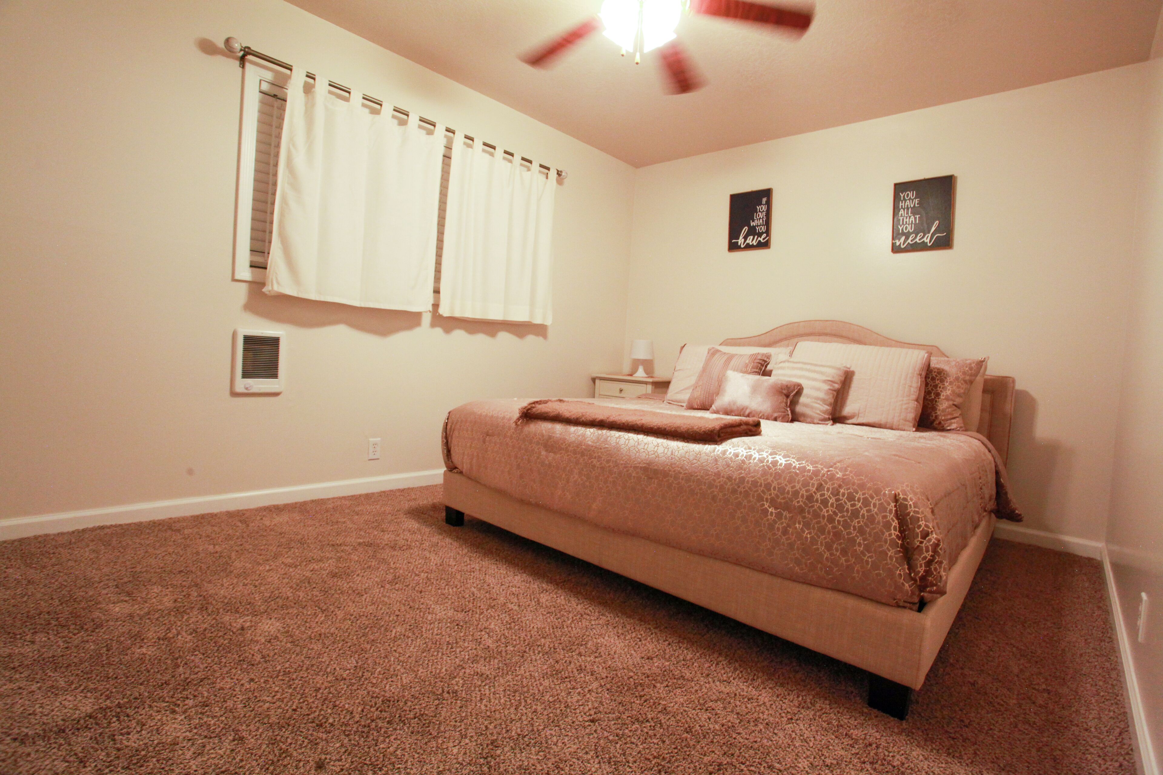 A bedroom with a bed, curtains, two wall art pieces, and a ceiling fan.